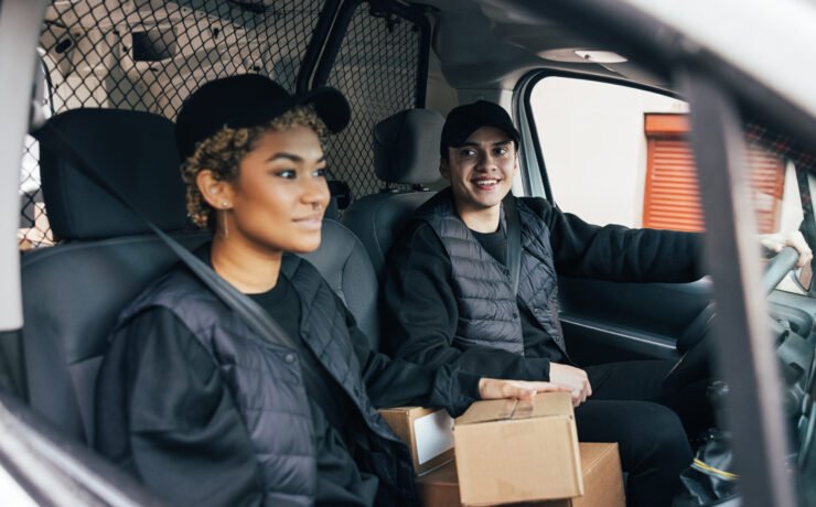 Delivery man looking away while sitting with a coworker in van