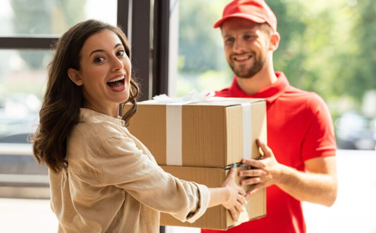 selective focus of happy woman receiving carton boxes from cheerful delivery man in cap